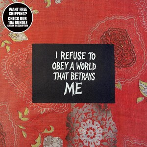 Puede incluir: Un parche rectangular negro con el texto blanco "I REFUSE TO OBEY A WORLD THAT BETRAYS ME". El parche está sobre una tela roja estampada. Un gráfico circular en la esquina superior izquierda dice "WANT FREE SHIPPING? CHECK OUR 10X BUNDLE LINK IN DESCRIPTION."