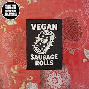Peut inclure: Écusson carré noir avec le texte blanc « VEGAN SAUSAGE ROLLS ». Le graphisme présente un rouleau de saucisse stylisé avec des lunettes de soleil. Un graphique circulaire en haut à gauche indique « WANT FREE SHIPPING? CHECK OUR 10X BUNDLE LINK IN DESCRIPTION ». Le fond est rouge.