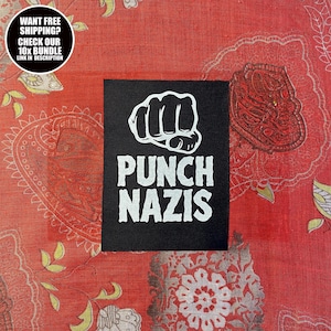 以下が含まれることがあります： 白抜きの拳のグラフィックと「PUNCH NAZIS」の文字がプリントされた黒い正方形のパッチ。赤い模様の生地の上に配置されています。左上には「WANT FREE SHIPPING? CHECK OUR 10X BUNDLE LINK IN DESCRIPTION」と書かれた円形のグラフィックがあります。