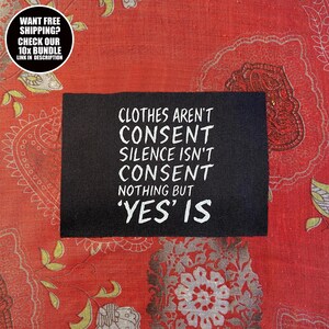 May include: A black rectangular sign with white text that reads "CLOTHES AREN'T CONSENT SILENCE ISN'T CONSENT NOTHING BUT 'YES' IS". The sign is on a red patterned fabric. A circular graphic in the upper left corner says "WANT FREE SHIPPING? CHECK OUR 10X BUNDLE LINK IN DESCRIPTION".