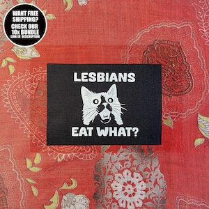 Könnte beinhalten: Ein schwarzer rechteckiger Aufnäher mit dem weißen Text "LESBIANS EAT WHAT?" und einer weißen Katzenillustration. Ein kreisförmiges Grafik im oberen linken Eck liest "WANT FREE SHIPPING? CHECK OUR 10X BUNDLE LINK IN DESCRIPTION."