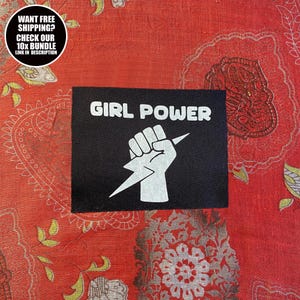 Peut inclure: Écusson noir avec les mots "GIRL POWER" en blanc, au-dessus d'un poing blanc tenant un éclair. L'écusson est posé sur un tissu rouge à motifs. Un graphique circulaire en haut à gauche indique "WANT FREE SHIPPING? CHECK OUR 10X BUNDLE LINK IN DESCRIPTION."