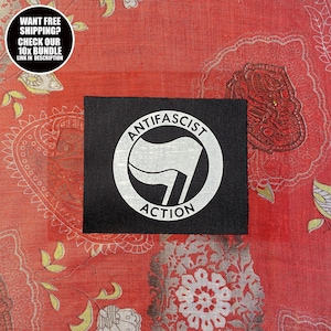 Op de afbeelding: Een zwarte patch met de witte woorden "ANTIFASCIST ACTION", rond een wit vlag-symbool. De patch is geplaatst tegen een rode achtergrond met patronen. Een cirkelvormige afbeelding linksboven leest "WANT FREE SHIPPING? CHECK OUR 10X BUNDLE LINK IN DESCRIPTION."