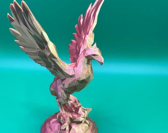 May include: A pink and gold 3D printed figurine of a phoenix with outstretched wings, standing on a circular base.