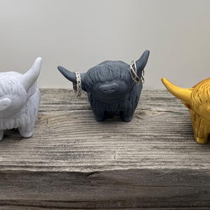 May include: Three Highland Cow ring holders, one white, one black, and one gold. Each cow is holding rings on its horns.