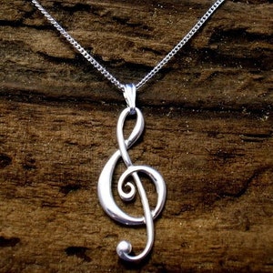 May include: A silver chain necklace with a treble clef pendant. The necklace is on a brown wooden surface.