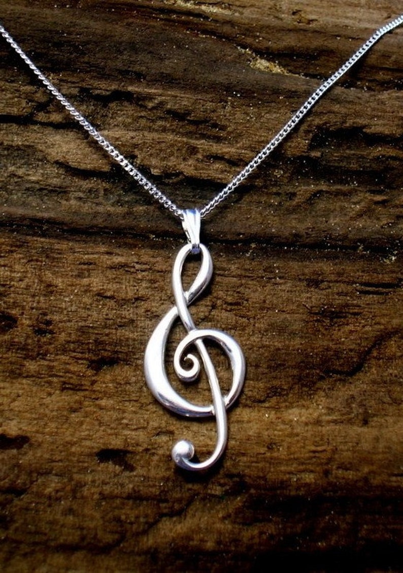 May include: A silver chain necklace with a treble clef pendant. The necklace is on a brown wooden surface.
