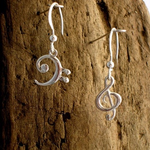 May include: A pair of silver earrings with musical note charms. One earring features a treble clef and the other a bass clef.