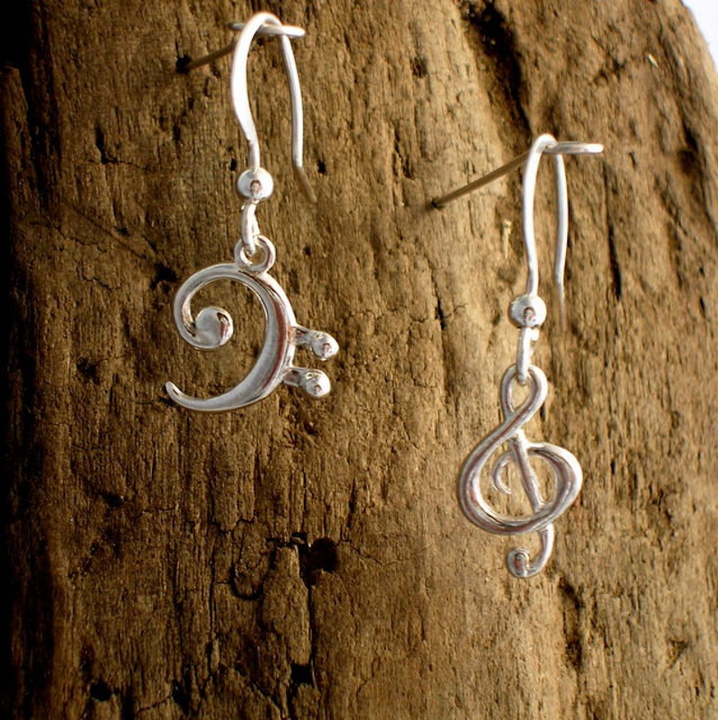 May include: A pair of silver earrings with musical note charms. One earring features a treble clef and the other a bass clef.