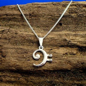May include: A silver necklace with a bass clef pendant. The necklace is on a wooden surface.