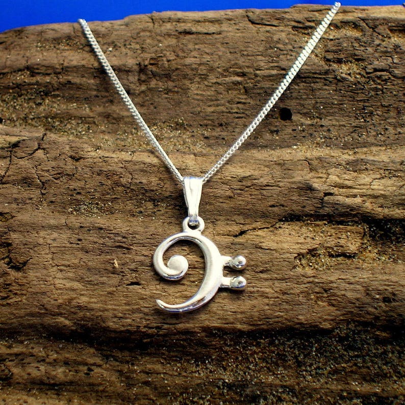 May include: A silver necklace with a bass clef pendant. The necklace is on a wooden surface.