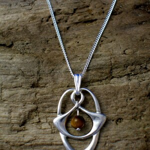 May include: A silver necklace with a pendant featuring a brown tiger's eye stone set in a silver frame. The pendant is shaped like a teardrop with a delicate design.