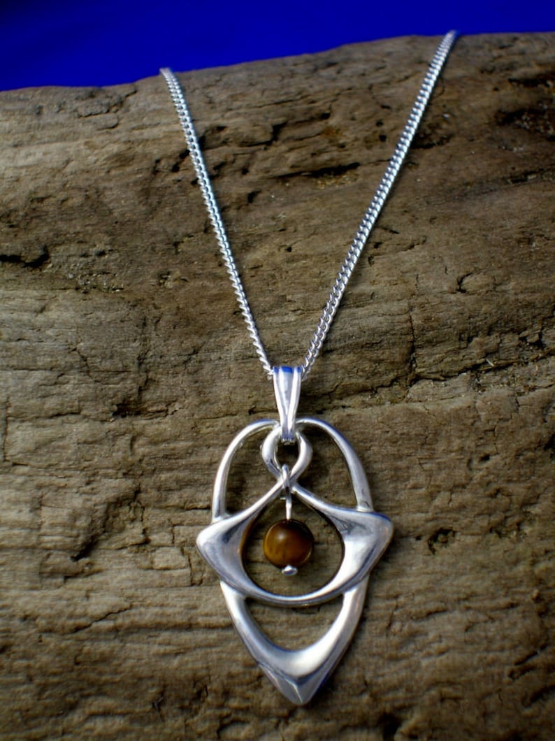 May include: A silver necklace with a pendant featuring a brown tiger's eye stone set in a silver frame. The pendant is shaped like a teardrop with a delicate design.