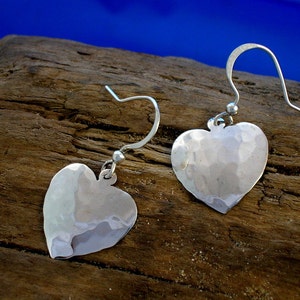 May include: A pair of silver heart-shaped earrings with a hammered texture. The earrings hang from a simple hook.