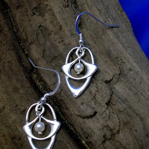 May include: A pair of silver earrings with a delicate, openwork design featuring a small pearl in the center of each earring.