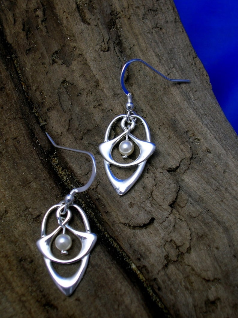 May include: A pair of silver earrings with a delicate, openwork design featuring a small pearl in the center of each earring.