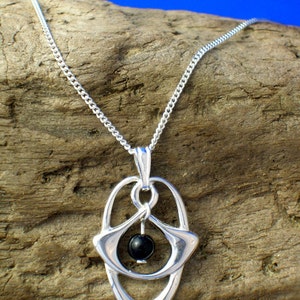 May include: A silver chain necklace with a pendant featuring a black gemstone surrounded by a silver design. The pendant is shaped like an oval with a pointed bottom.