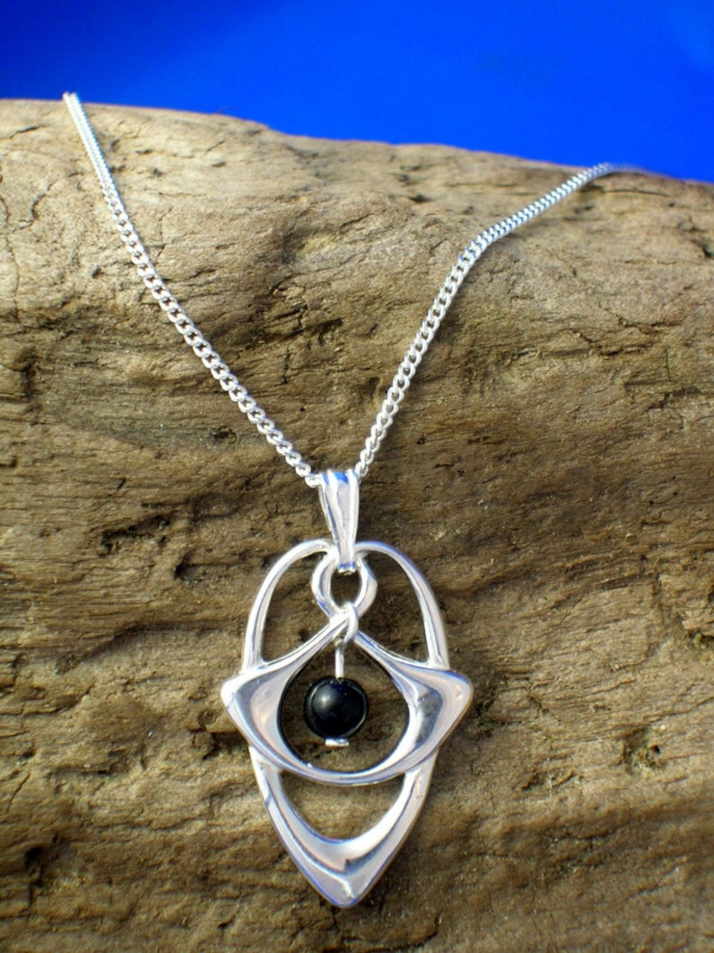 May include: A silver chain necklace with a pendant featuring a black gemstone surrounded by a silver design. The pendant is shaped like an oval with a pointed bottom.