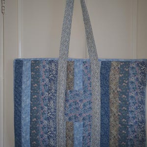 May include: A blue and white patchwork tote bag with a floral pattern. The bag has two long straps and is made of fabric.