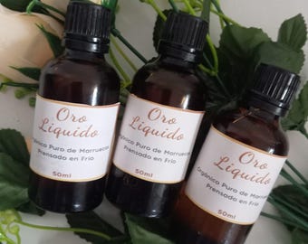 May include: Three amber glass bottles with black caps and white labels. The labels read "Oro Liquido" and contain text in Spanish about the product being organic, pure, and cold-pressed. Each bottle contains 50 ml of liquid.