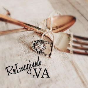 May include: A silver-toned pendant shaped like a heart, crafted from a repurposed spoon handle featuring an embossed grape cluster design. The pendant hangs from a thin chain, positioned near a metal fork. The text ReImagined in VA is visible.
