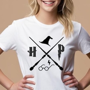 以下が含まれることがあります： 白いTシャツ。黒いグラフィックデザインで、文字「HP」、魔法使いの帽子、交差した杖、稲妻、眼鏡が描かれています。デザインは中央に配置されています。