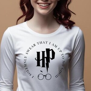 May include: White long-sleeve shirt featuring a black graphic design from the Harry Potter series. The design includes the letters "HP", a lightning bolt, glasses, and the phrase "I SOLEMNLY SWEAR THAT I AM UP TO NO GOOD" in a circular pattern.
