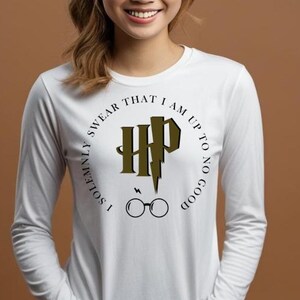 以下が含まれることがあります： 白い長袖シャツ。円形のデザインで、「I solemnly swear that I am up to no good」の文字がメガネと稲妻のロゴの周りに書かれています。ファンアイテムです。