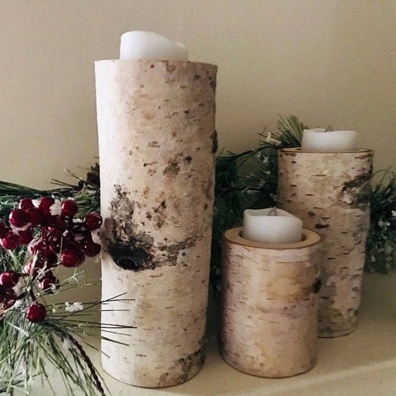 May include: Three birch bark candle holders with white candles. The candle holders are different sizes and are arranged on a white surface.