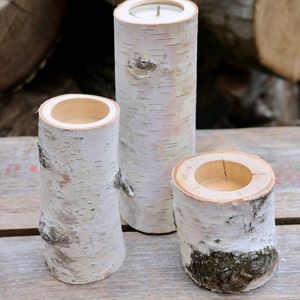 May include: Three birch bark candle holders, each with a different size opening. The candle holders are on a wooden surface.