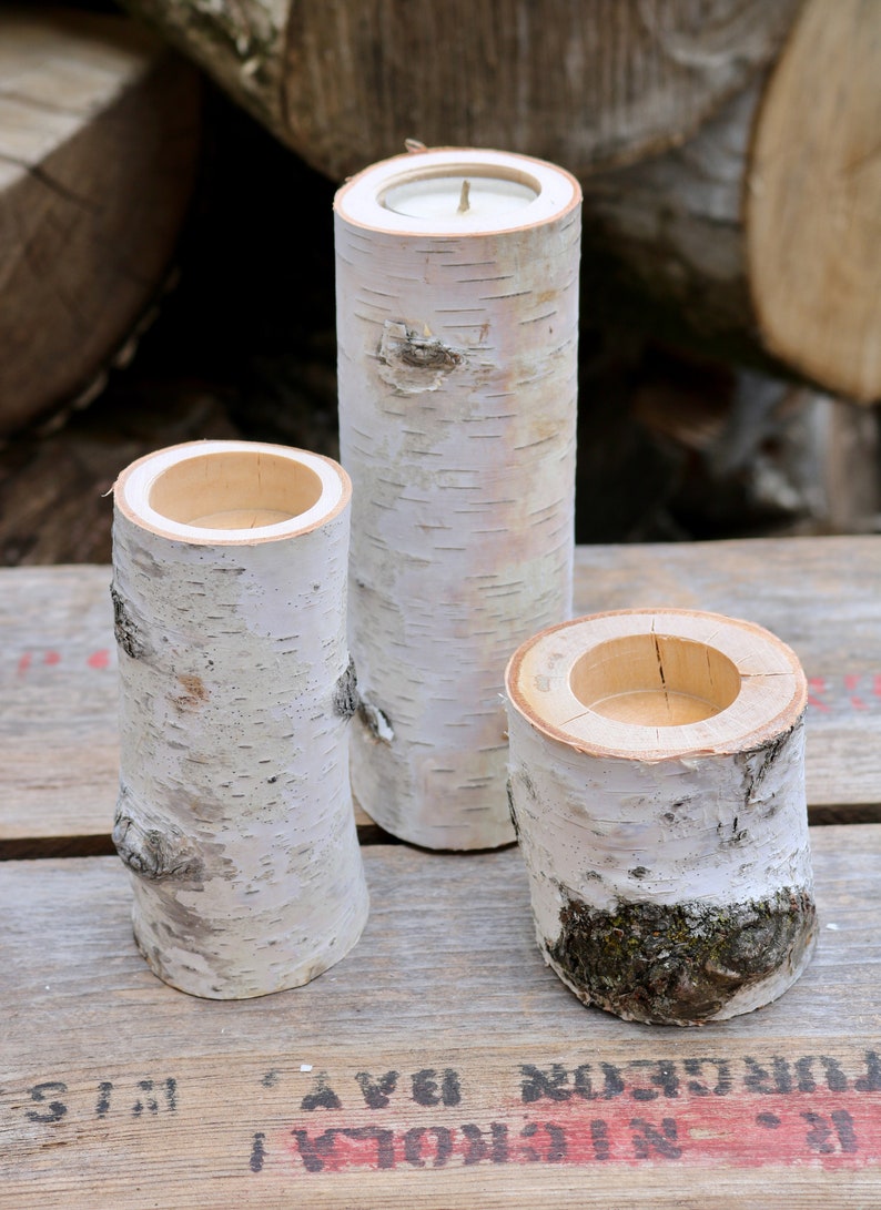 May include: Three birch bark candle holders, each with a different size opening. The candle holders are on a wooden surface.