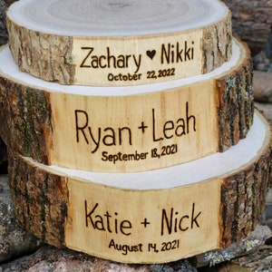 K&ouml;nnte beinhalten: Drei Holzkuchenst&auml;nder mit Rindenkanten, &uuml;bereinander gestapelt. Der obere St&auml;nder ist mit "Zachary Nikki October 22, 2022" graviert. Der mittlere St&auml;nder ist mit "Ryan + Leah September 18, 2021" graviert. Der untere St&auml;nder ist mit "Katie + Nick August 14, 2021" graviert.