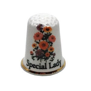 May include: White ceramic thimble with a floral design in orange, yellow, and purple. The thimble has the words "Special Lady" in black script with a gold rim.