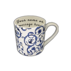 May include: White ceramic mug with a blue floral pattern. The mug has a curved handle and the text "Your name or message here" inside the rim. The design features swirling blue vines and flowers.