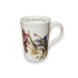 May include: White ceramic mug with a floral design featuring purple, blue, and cream-coloured irises. The mug has a curved handle and the text "Iris's Special Cup" printed on the inside rim.