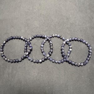 May include: Four dark blue gemstone bracelets with silver flecks. The bracelets are made of small, round beads and are stacked on top of each other.