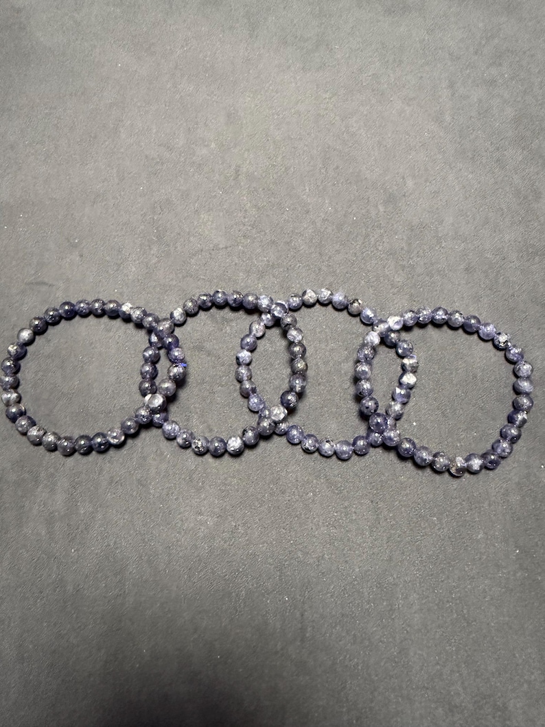 May include: Four dark blue gemstone bracelets with silver flecks. The bracelets are made of small, round beads and are stacked on top of each other.