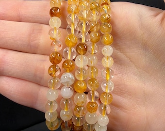 May include: Four elastic bracelets composed of round, polished beads in varying shades of translucent yellow, amber, and clear quartz. Each bead features unique internal golden rutile inclusions, creating a natural, multi-tonal appearance.