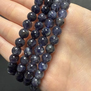 May include: Three strands of dark blue gemstone beads, each strand is a bracelet with round beads. The beads have a speckled appearance.
