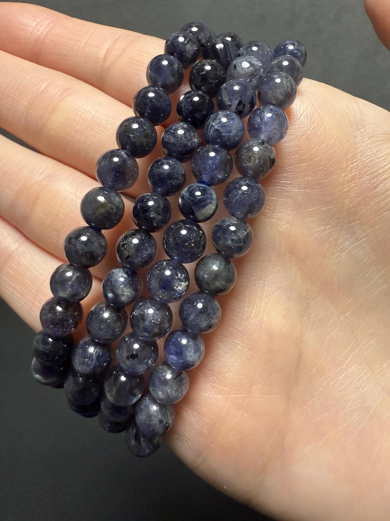 May include: Three strands of dark blue gemstone beads, each strand is a bracelet with round beads. The beads have a speckled appearance.