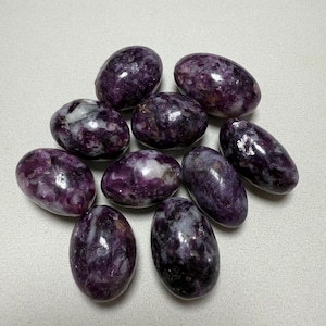 May include: A collection of polished, oval-shaped stones in shades of deep purple and white. The stones have a smooth, glossy surface and vary slightly in size and color, creating a natural, organic aesthetic. These stones are ideal for jewelry making or collecting.
