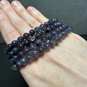 May include: A stack of four dark blue gemstone bracelets with round beads. The bracelets are made of natural stones and have a sparkly, iridescent finish.