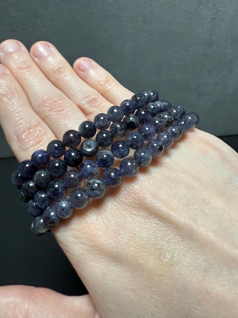 May include: A stack of four dark blue gemstone bracelets with round beads. The bracelets are made of natural stones and have a sparkly, iridescent finish.
