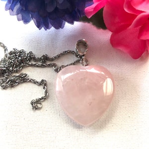 May include: A silver chain necklace with a large, light pink heart-shaped pendant made of rose quartz.