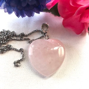 May include: A silver chain necklace with a rose quartz heart pendant. The heart is a light pink color and has a smooth, polished finish.