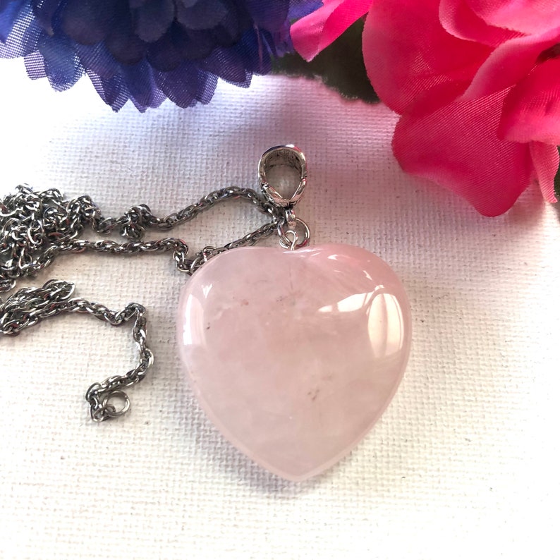 May include: A silver chain necklace with a rose quartz heart pendant. The heart is a light pink color and has a smooth, polished finish.