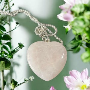 May include: A delicate silver chain necklace with a heart-shaped rose quartz pendant. The pendant is a light pink color and has a smooth, polished finish.