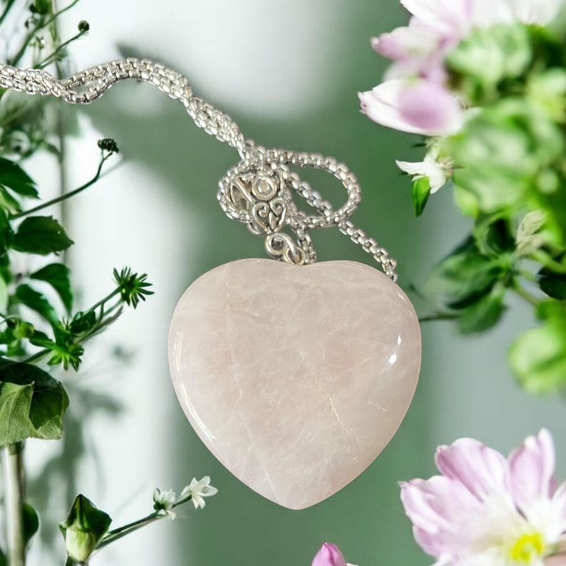 May include: A delicate silver chain necklace with a heart-shaped rose quartz pendant. The pendant is a light pink color and has a smooth, polished finish.
