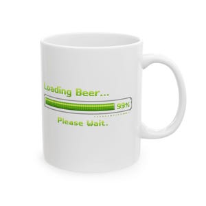 Könnte beinhalten: Weißer Keramikbecher mit gebogenem Henkel. Der Becher zeigt den Text "Loading Beer..." über einem grünen Fortschrittsbalken bei 99% und "Please Wait." darunter. Ein humorvolles Design.