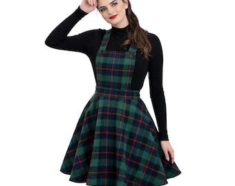 Può includere: Un abito con gonna a quadri verdi, blu navy e rossi con gonna svasata e spalline abbottonate. L'abito è abbinato a un top nero a maniche lunghe. Uno stile classico di ispirazione vintage.